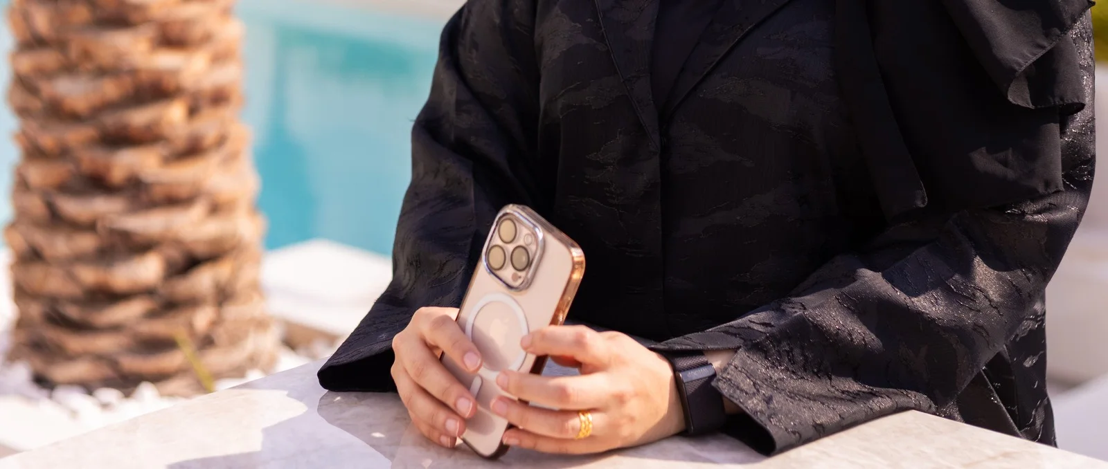 A hand holding a phone at a poolside marble table in Dubai, the mobile-first world Arabic users search from